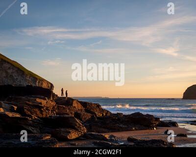 Silhouette di un surfista che cammina lungo una spiaggia in Cornovaglia al tramonto Foto Stock