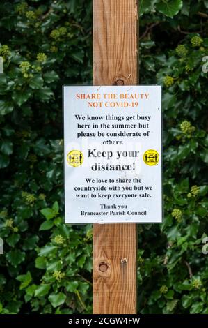 Un segno che incoraggia l'allontanamento sociale durante la pandemia di coronavirus. A Brancaster sulla costa nord del Norfolk. Foto Stock