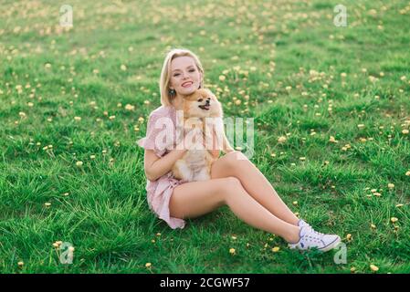 Ritratto di una giovane donna glamour che indossa un vestito rosa che tiene il suo spitz pomeranian carino sulle mani. . Amicizia tra cani e esseri umani. Foto Stock