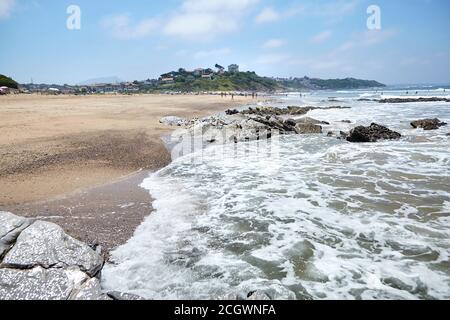 Spiaggia di sabbia di Bidart, Francia. Pietre affilate e acqua dell'oceano. Giornata estiva soleggiata con cielo blu Foto Stock