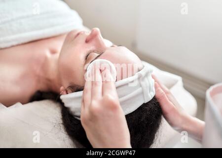 Mani femminili di estetista deterge la pelle con tamponi di cotone. Cura della pelle del viso. La donna caucasica su una procedura di cosmetologia. Visita al salone di bellezza Foto Stock