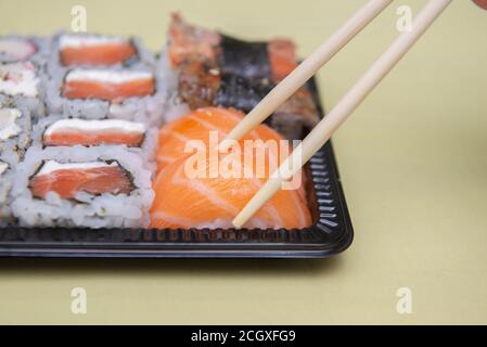 Primo piano di bastoncini di pollo che raccolgono i niguiri di salmone dal vassoio di plastica nero - cibo giapponese consegnato. Messa a fuoco selettiva. Foto Stock