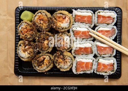Primo piano di sushi assortiti con i chopsticks sul tavolo. Vassoio nero con rotolo caldo e sushi di salmone con formaggio cremoso. Cibo delizioso consegnato. Foto Stock