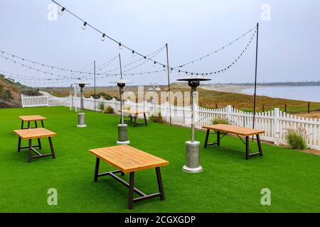 Posti a sedere all'aperto in un ristorante fronte spiaggia vuoto a causa della pandemia, Half Moon Bay vicino a San Francisco, Oceano Pacifico sullo sfondo in una giornata foggosa Foto Stock