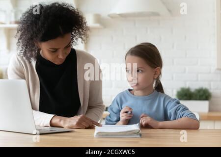 Donna biraciale focalizzata che aiuta il bambino piccolo a studiare a casa. Foto Stock