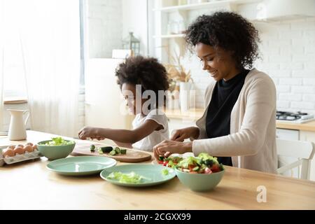 Sorridente giovane etnia africana che cucina con piccola figlia. Foto Stock