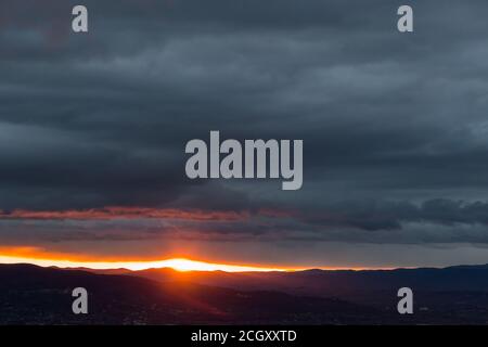 Tramonto sulle montagne e sulla valle, con il sole che scende attraverso un buco nelle nuvole Foto Stock