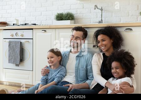 Famiglia multirazziale sorridente seduta al piano in cucina moderna ristrutturata. Foto Stock