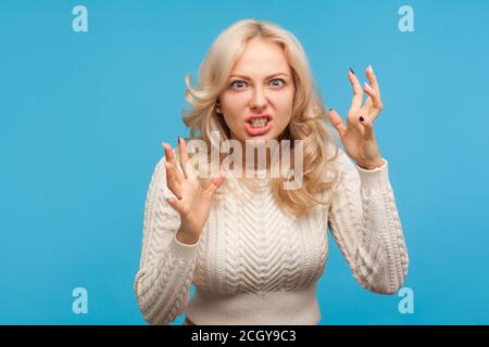 Donna bionda aggressiva stressata che sostiene e diventa denti pazzi clenching, pazza furiosa donna in depressione. Studio al coperto isolato su sfondo blu Foto Stock