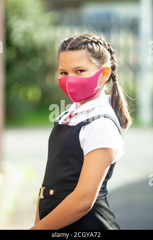 Una studentessa di dieci anni in una divisa scolastica con i capelli in trecce e indossando una maschera rosa. Foto Stock