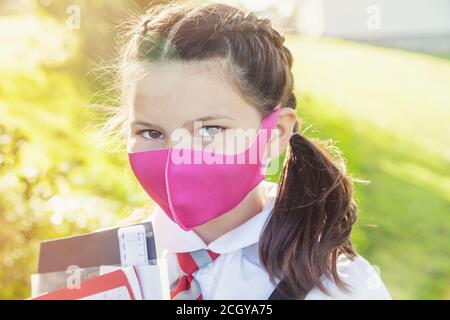 Primo piano della faccia di una ragazza di 10 anni con i suoi capelli in trecce e indossare una maschera rosa. Foto Stock