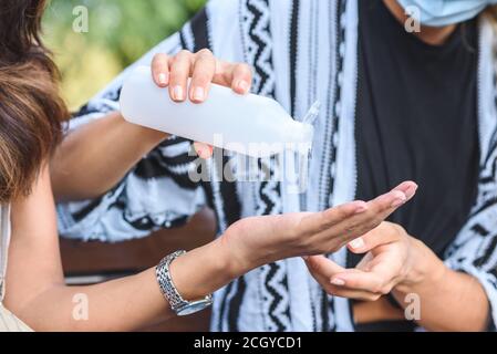 le mani di una giovane donna caucasica che condivide il gel igienico con un amico indiano per strada Foto Stock