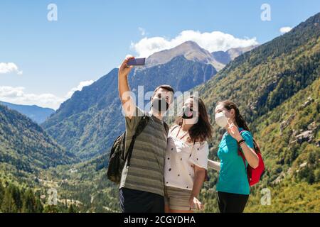 Foto d'inventario di un gruppo di tre amici che indossano maschere e prendere un selfie mentre si gode le montagne e bello scenario Foto Stock