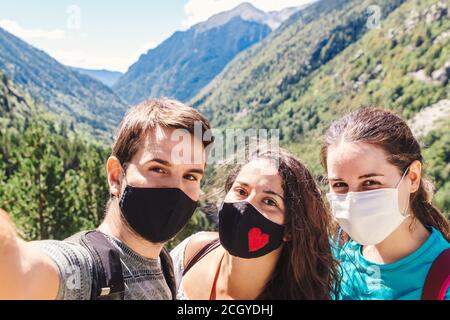 Scatta foto di un selfie di gruppo indossando maschere e godendosi le montagne e il paesaggio in una giornata di sole Foto Stock