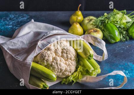 Verdure verdi e frutta in una borsa di tela su uno sfondo blu di cemento. Il concetto di alimentazione sana e dieta. Foto Stock