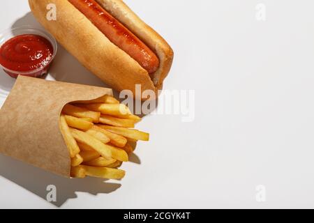 Fast food isolato su sfondo bianco. Patatine fritte in eco pack, hot dog e ketchup in contenitore Foto Stock