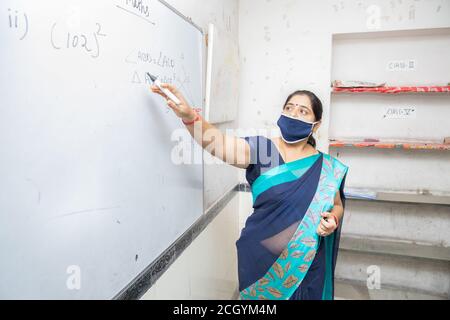 Insegnante femminile che indossa maschera e insegna che punta sulla lavagna in classe, scuola indiana classe di istruzione durante il covid19 pandemic, nuovo normale, copia spa Foto Stock