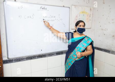 Insegnante femminile che indossa maschera e saree insegnano matematica su lavagna bianca in classe, scuola indiana classe di istruzione durante il cofid19 pandemia, nuova normalità Foto Stock