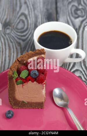 Un pezzo di torta al cioccolato senza forno con formaggio cremoso. Guarnito con lamponi, mirtilli e foglie di menta. Nelle vicinanze si trova una tazza di caffè. Sulla Foto Stock