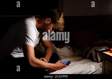 Un giovane pazzo guarda il suo telefono nel suo bedrom di notte Foto Stock