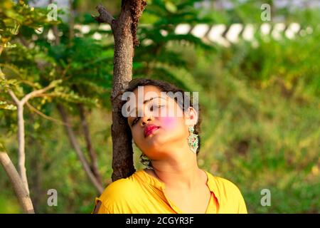 Un bel modello femminile indiano posa in una foto con l'aiuto di un albero in piedi sulla strada Foto Stock