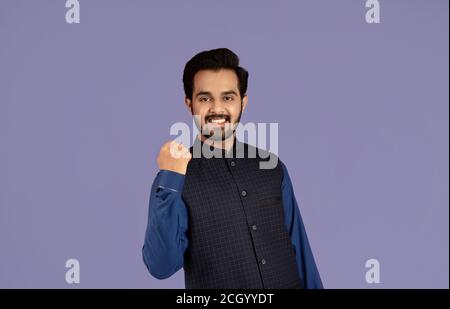 Attraente ragazzo indiano con sorriso sul suo viso facendo sì gesto su sfondo lilla Foto Stock