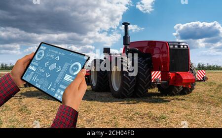 Un agricoltore con tavoletta digitale controlla un autonomo del trattore su una smart farm Foto Stock