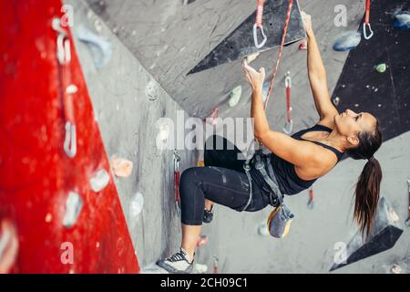 Sportivo da donna d'affari di successo essendo occupato al suo hobby-bouldering. Ben accessoriate donna formazione in un colorato palestra di arrampicata, preparazione per l'estate moun Foto Stock