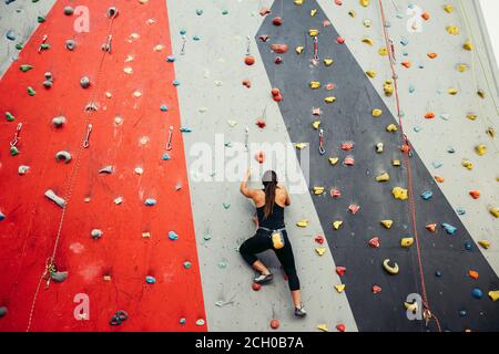 Studente sportivo donna vestita di nero abbigliamento sportivo, salendo sul muro di allenamento in palestra, in vista posteriore Ragazza alleviare lo stress dopo gli esami intensivi tim Foto Stock