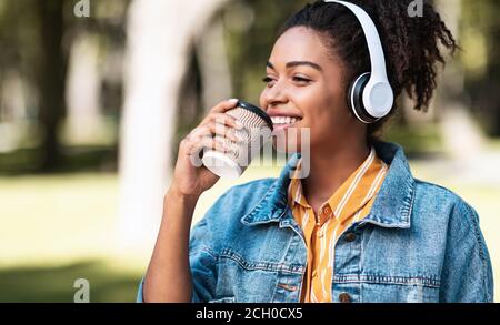 Black Girl con cuffie che hanno caffè godendo Weekend a Park Foto Stock