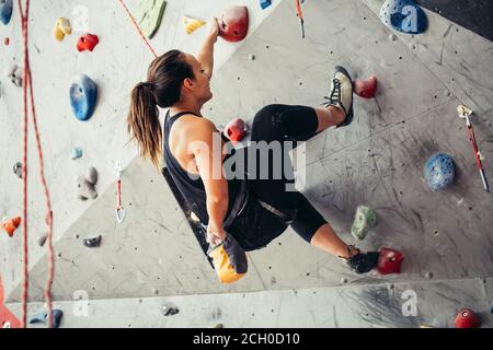 Sportivo da donna d'affari di successo essendo occupato al suo hobby-bouldering. Ben accessoriate donna formazione in un colorato palestra di arrampicata, preparazione per l'estate moun Foto Stock