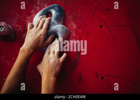 Primo piano di donne arrampicatrici mani sulla parete rossa durante il bouldering. Allenati in palestra per arrampicata, primo piano Foto Stock