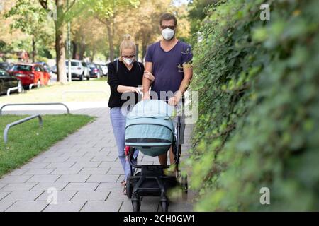 Preoccupato giovane genitore che cammina su una strada vuota con passeggino che indossa maschere mediche per proteggerli dal virus corona. Vita di distanza sociale durante Foto Stock