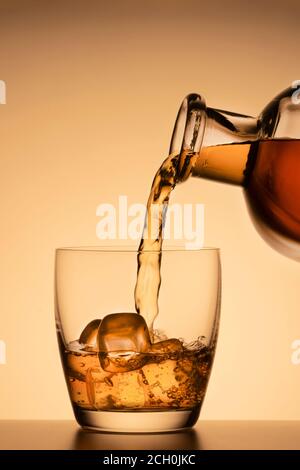 Bevanda alcolica, versata da un bicchiere da una bottiglia su sfondo oro arancio. Whisky, cognac o scotch borbonico Foto Stock