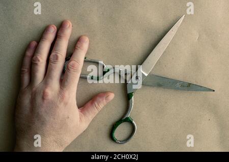 La mano di un uomo caucasico adulto poggia su una vecchia forbici di metallo. Attrezzi fatti a mano retrò di un sarto. Manodopera manuale. Artigianato. Vista dall'alto ad angolo. Foto Stock