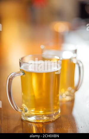 Tazza trasparente di birra chiara su un tavolo di legno con il suo riflesso nel mirrow. Foto Stock