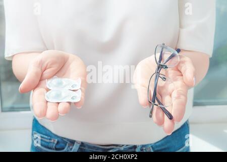 Donna che tiene gli occhiali e la lente di contatto su sfondo bianco, fuoco selettivo sugli occhiali, miopia e concetto di problema di vista Foto Stock