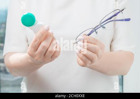 donna che sceglie tra occhiali e lenti a contatto. la donna tiene gli occhiali in una mano e un giorno lenti a contatto nell'altra. miopia e vista Foto Stock