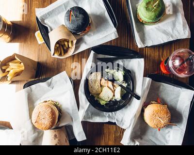 Hamburger di diverse colorazioni con insalata di verdure, patatine fritte su tavola di legno, vista dall'alto. Foto Stock