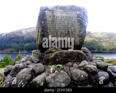 Un tributo floreale al memoriale Robert the Bruce (conte di Carrick), vicino a Loch Troon, Galloway (fotografia del 2020). La Battaglia di Glen Trool ebbe luogo nella prima Guerra d'Indipendenza scozzese, combattuta nell'aprile 1307. Glen Trool è un glen stretto nella zona meridionale di Galloway, in Scozia, in cui Loch Trool (dietro il monumento) è situato. Mentre i soldati inglesi si avvicinarono alla stretta glen in un unico file, gli uomini di Bruce li scagliarono massi e frecce verso il basso . I soldati inglesi furono uccisi o ritirati e Bruce fu vittorioso. Foto Stock