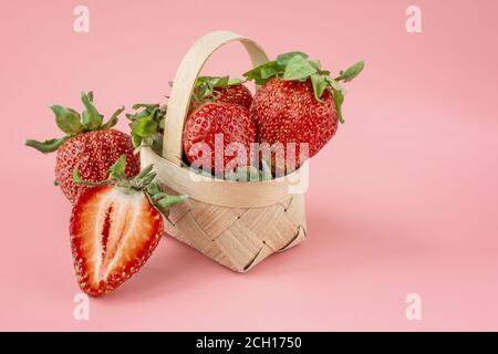 fragole grandi in un piccolo cesto su sfondo rosa chiaro. Fragole biologiche fresche in un piccolo cesto. Cibo sano estivo. Foto Stock