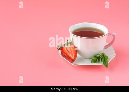 tazza di tè bianco con menta e fragole rosse mature su sfondo rosa. vista dall'alto. primo piano Foto Stock