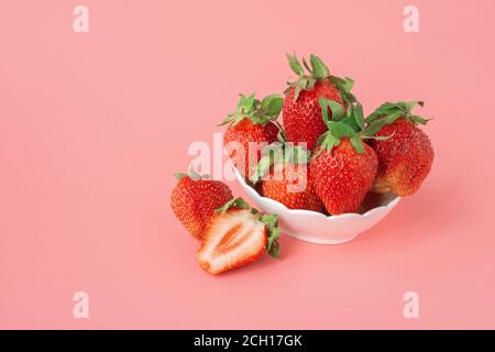 fragole rosse mature in un recipiente su sfondo rosa. Raccogliere le fragole fresche nel recipiente. Fragole fresche mature in una ciotola bianca sul dorso rosa Foto Stock