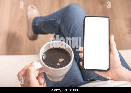 cellulare mockup. Immagine mockup delle mani di donna che tengono il telefono cellulare con schermo vuoto e tazza di caffè a casa Foto Stock