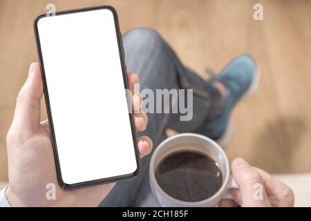 Immagine mockup di un uomo che tiene una mano telefono cellulare nero con schermo da tavolo vuoto. Primo piano mano che tiene il telefono cellulare schermo vuoto in caffetteria Foto Stock