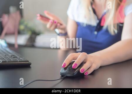 Donna che usa il mouse del computer con il desktop al tavolo, closeup. Donna lavora su computer portatile, mano che tiene mobile smartphone. Donna con chiodi rossi holdin Foto Stock