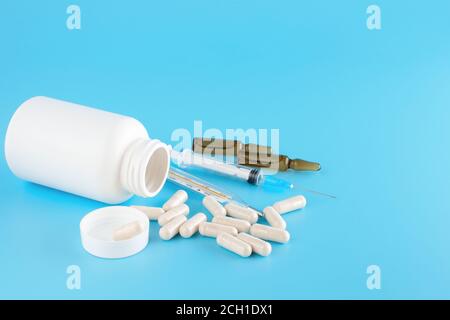 Pillole, capsule, siringhe, contenitori medici bianchi, ampolle e termometro medico al mercurio su sfondo blu. Flaconcino medico per iniezione con un Sir Foto Stock