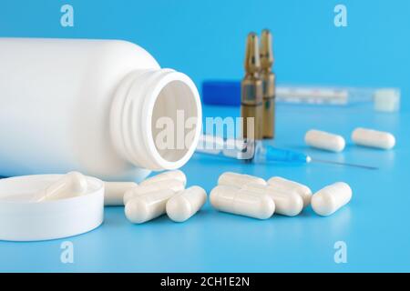 Le pillole fuoriescono dal contenitore bianco. Contenitori medici, pillole, siringhe, fiale per preparazioni iniettabili su sfondo medico blu. Medicinali diversi Foto Stock