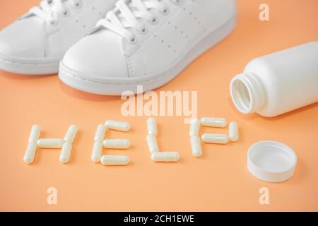 Sneakers e pillole. Capsule di condroitina e sneakers. L'aiuto di parola è allineato con le capsule o le pillole su sfondo luminoso. Farmaci di supporto per gli attiviti Foto Stock