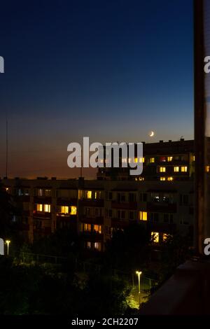 Luna crescente ceretta che si erge su blocchi di appartamenti a nightfall, vista urbana, paesaggio urbano Foto Stock